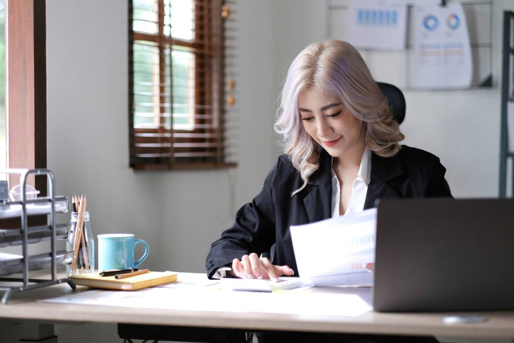 beautiful asian businesswoman analyzes charts using laptop calculator in office